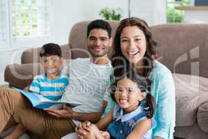 Portrait of parents and children sitting on sofa and reading book
