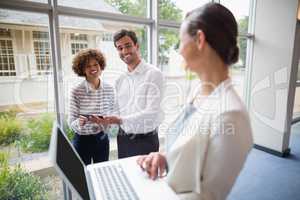 Businesswoman holding laptop and interacting with colleagues