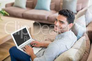 Man sitting on sofa and using laptop in living room at home