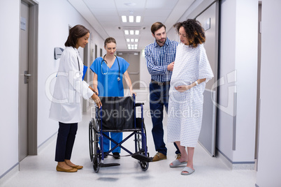 Man and doctors assisting pregnant woman to sit on wheelchair