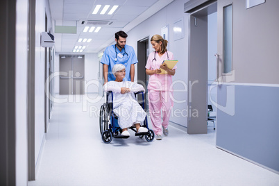 Male and female doctor interacting with female senior patient on wheelchair in corridor