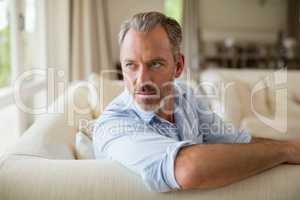 Thoughtful man sitting on sofa in living room