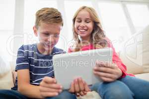 Siblings using digital tablet on sofa in living room