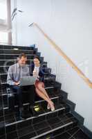 Businessman and woman sitting on steps using laptop and digital tablet