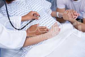 Doctor examining pregnant womans belly with stethoscope in ward
