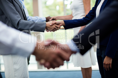 Mid section of business executives shaking hands with each other