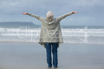 Senior woman standing with arms outstretched on the beach
