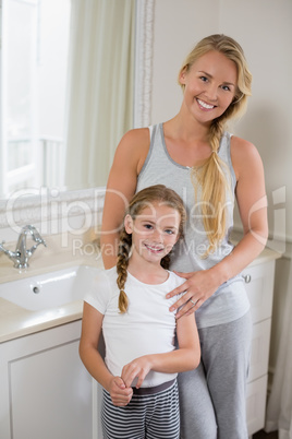 Smiling mother and daughter standing in bathroom