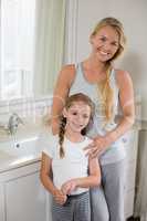 Smiling mother and daughter standing in bathroom