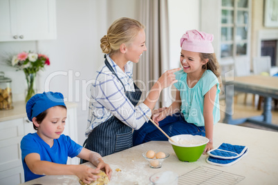 Mother and kids having fun while making dough in kitchen