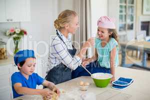 Mother and kids having fun while making dough in kitchen