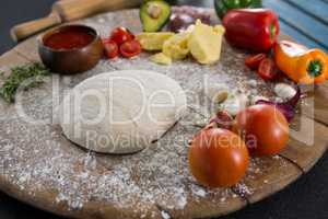 Various ingredients with pizza dough and flour on rolling board