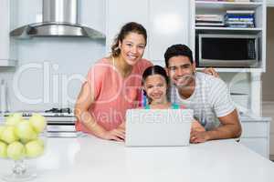 Parents and daughter using laptop in kitchen at home