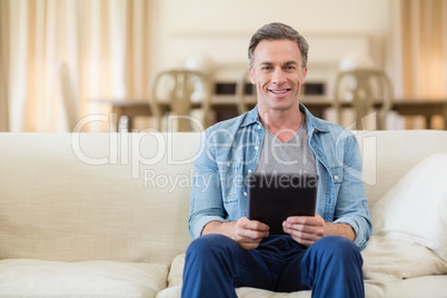 Portrait of man sitting on sofa and using digital tablet in living room