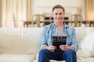 Portrait of man sitting on sofa and using digital tablet in living room