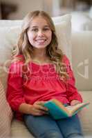 Smiling girl reading a book on sofa in living room