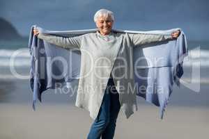 Smiling senior woman wrapped in shawl at beach