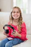 Smiling cute girl sitting on sofa with headphones and mobile phone in living room