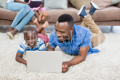 Father and daughter lying on rug and using laptop