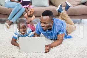 Father and daughter lying on rug and using laptop