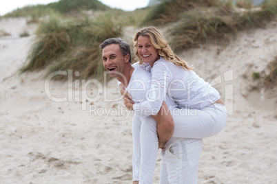 Mature man giving piggyback ride to woman on beach