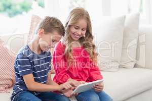 Siblings using digital tablet on sofa in living room