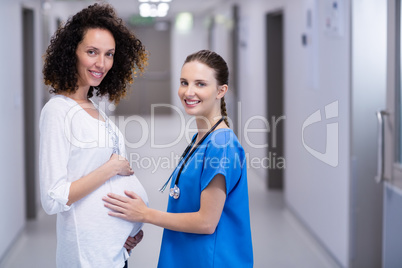 Portrait of doctor touching pregnant womans belly in corridor