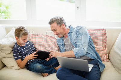 Father and son using laptop and digital tablet in living room