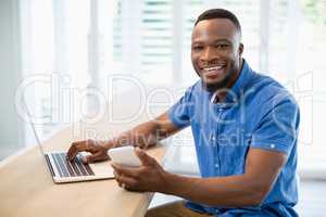 Man using laptop and mobile phone in living room at home