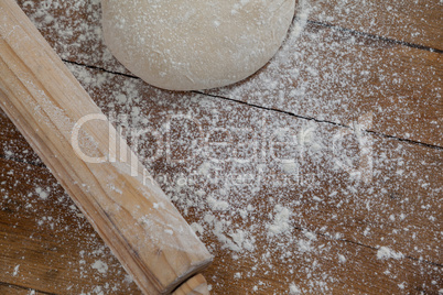 Rolling pin with pizza dough and flour on wooden plank