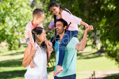 Parents carrying their children on shoulder in park