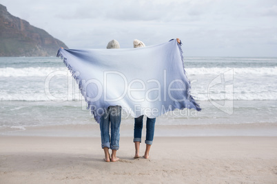 Mature couple holding shawl behind back on the beach