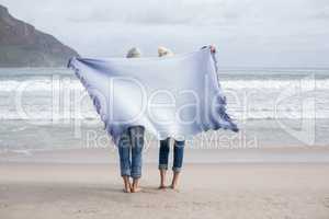 Mature couple holding shawl behind back on the beach