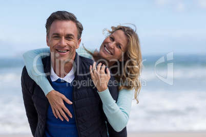 Mature man giving piggyback ride to woman on beach