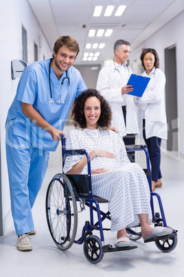 Portrait of doctor pushing a pregnant woman on wheelchair