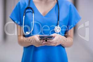 Mid section of female doctor using mobile phone in corridor
