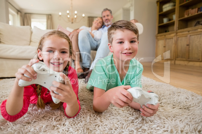 Siblings lying on rug and playing video game