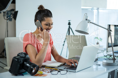 Female photographer working over laptop while talking on mobile phone