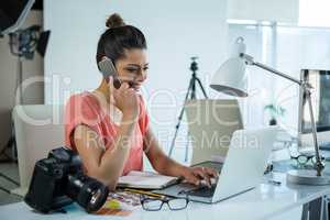 Female photographer working over laptop while talking on mobile phone