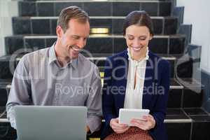 Businessman and woman sitting on steps using laptop and digital tablet