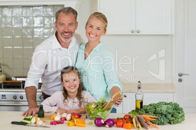 Smiling parents and daughter preparing vegetable salad in kitchen
