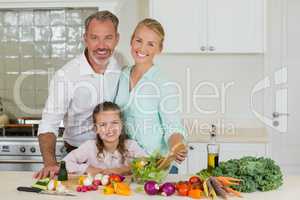 Smiling parents and daughter preparing vegetable salad in kitchen