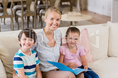 Mother and kids sitting on sofa with book in living room
