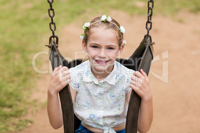 Happy girl sitting on a swing in park