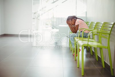 Upset girl sitting on chair in corridor