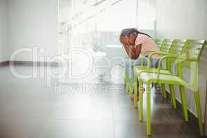 Upset girl sitting on chair in corridor