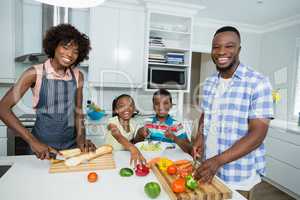 Parents and kids preparing salad while father using digital tablet in kitchen at home