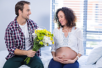 Man offering bunch of flowers to his pregnant woman in ward