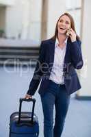 Businesswoman carrying luggage and talking on mobile phone