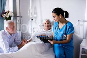 Female doctor discussing with senior couple over a report in the ward